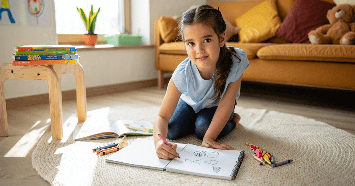 Child drawing in a sketchbook on the floor with crayons.